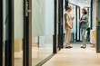 © DragonImages - Middle-aged man and mature woman chatting during coffee break standing in office building corridor, horizontal long shot
