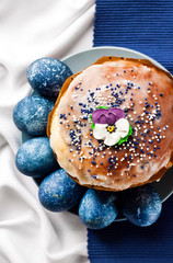 Wall Mural - Easter cake decorated with sugar flower and blue colored eggs on a plate on white and blue cloth background