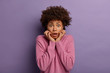 Omg, how scary! Freak out frightened ethnic young woman stands anxious, afraids of something terrible, hears bad news, dressed casually, stands against vivid purple background, shakes from fear