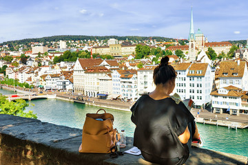 Poster - Girl sitting on Lindenhof hill and looking into a guide book in Zurich, Switzerland. Limmatquai and Predigerkirche on the background