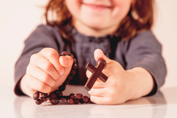 Developing the spiritual and religious life of child. Little cute girl praying with wooden rosary.