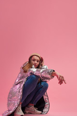 a cool girl in a shiny silver down jacket and a knitted hat squatted down,