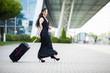 Smiling female passenger proceeding pulling suitcase through airport