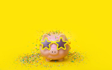 A pink piggy bank in fun glasses at a party. Yellow background.