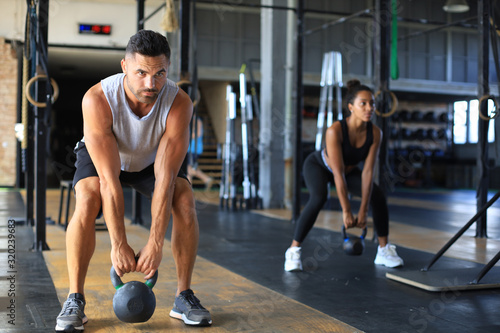 Cuadros en Lienzo Fit and muscular couple focused on lifting a dumbbell during an exercise class in a gym