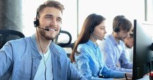 Portrait Of Call Center Worker Accompanied By His Team. Smiling Customer Support Operator At Work.