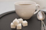 Fototapeta Dinusie - Morning tea in a white cup with sugar cubes on a black tray.