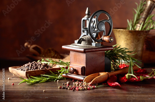 Fotomural Vintage pepper mill with kitchen utensils, spices and rosemary on a old wooden table