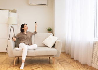 Young woman switching on air conditioning at her home