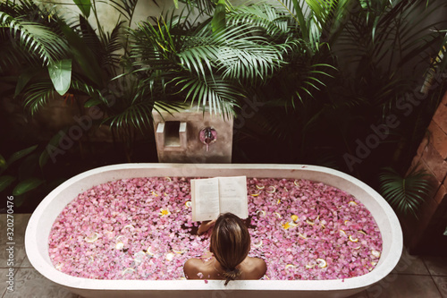 Woman reading book while relaxing in bath tub with flower petals © Alena Ozerova