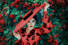 Happy Women's Day Holiday March 8. Portrait Stylish Spring Woman Retro Makeup Red Lips Sexy Cat Eyes. St Valentine's Party Hat Wide-brimmed. Bright Roses Flowering Bushes Green Leaves Garden Park Tree