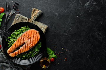 Baked salmon steak with green beans on a black plate. Top view. Free copy space.