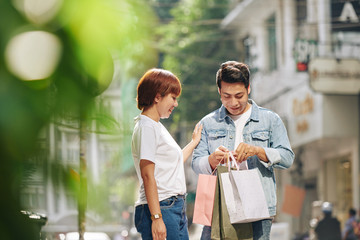 Poster - Horizontal shot of positive Asian man and woman spending time together walking with shopping bags outdoors