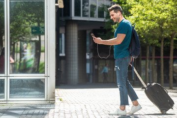 Wall Mural - side portrait of young travel man walking with suitcase and mobile phone