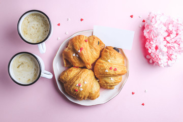 Valentine's day concept with two cups of coffee, almond croissant on pink plate on pink background. Top view,copy space. Romantic holiday