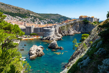 The walled city of Dubrovnik, Croatia taken from Fort Lovrijenac. The turquoise clear water of the Adriatic surrounds the ancient walled city, kayaks and a sailing boat provides scale.