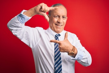 Wall Mural - Senior handsome businessman wearing elegant tie standing over isolated red background smiling making frame with hands and fingers with happy face. Creativity and photography concept.