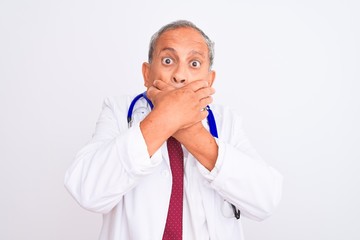 Canvas Print - Senior grey-haired doctor man wearing stethoscope standing over isolated white background shocked covering mouth with hands for mistake. Secret concept.