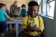 © wavebreak3 - Schoolboy standing holding a seedling plant in a jar of earth in an elementary school classroom
