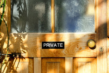 Private Sign Seen Attached To An Old, Wooden Door Located In A Large Glass House. The Rustic Wooden Texture Of The Wood And Ornate Brass Door Knob Is Seen With The Sun Casting Shadows.