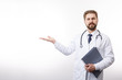 © Kuz Production - Handsome bearded doctor with folder and stethoscope keeping his hand stretched aside with open palm up isolated white background copyspace