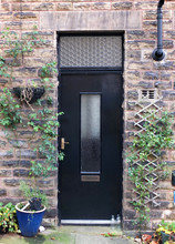 A Black Door In A Typical Traditional Yorkshire House With Stone Walls Surrounded By Plants In Pots And Milk Bottles