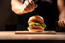 Make It Professional, Home Made Hamburger Made By White Sesame Bun, Tomato Slice, Salad, Cheese, Grilled Meat And Onion On Wooden Tray Wooden Table With Cooking Decorate Chef Hand Isolate In Dark