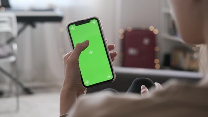 Close up of a woman's hand holding a mobile telephone with a vertical green screen indoors. Touch screen hand gestures. Use smart phone for browsing social networks and communicating closeup