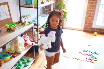 Beautiful toddler girl holding cute unicorn doll at kindergarten