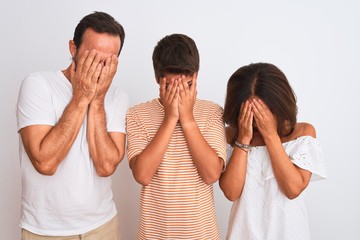 Canvas Print - Family of three, mother, father and son standing over white isolated background with sad expression covering face with hands while crying. Depression concept.