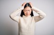 © Krakenimages.com - Young beautiful asian woman wearing casual sweater standing over isolated background suffering from headache desperate and stressed because pain and migraine. Hands on head.