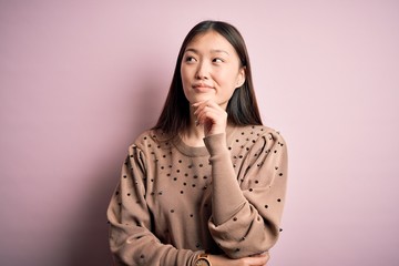 Wall Mural - Young beautiful asian woman wearing fashion and elegant sweater over pink solated background with hand on chin thinking about question, pensive expression. Smiling and thoughtful face. Doubt concept.