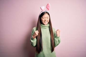 Sticker - Young asian woman wearing cute easter bunny ears over pink background excited for success with arms raised and eyes closed celebrating victory smiling. Winner concept.