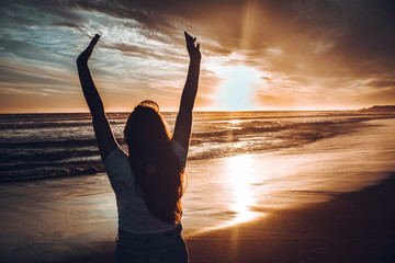 mujer con las manos en alto en la playa atardecer