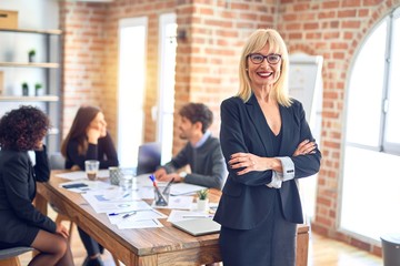 Group of business workers working together. Middle age beautiful woman standing smiling happy looking at the camera at the office