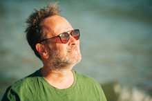Outdoor Portrait Of Happy Middle Age Man Enjoying Nice Sunny Day On The Beach, Wearing Green T-shirt And Sunglasses