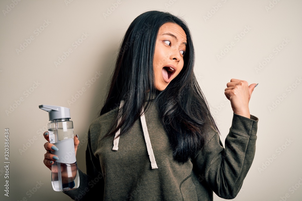 Young beautiful chinese sportswoman holding bottle of water over ...