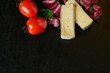 © Oleg - Cheese delikatessen closeup on black stone desk surface. Camembert or brie circle in brown kraft paper decorated with basil and pieces of cherry tomatoes, top view image with copy space