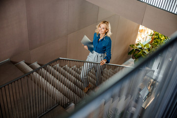 Cheerful lady with laptop walking up the stairs