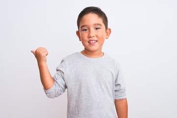 Canvas Print - Beautiful kid boy wearing grey casual t-shirt standing over isolated white background smiling with happy face looking and pointing to the side with thumb up.