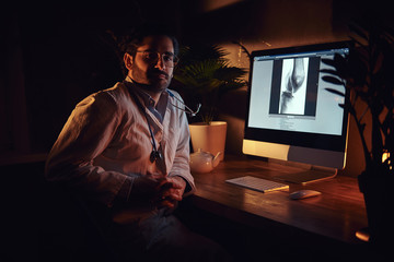 Wall Mural - Pensive dilligent intern is working at late night shift at his office using a computer.