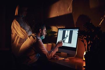 Wall Mural - At the dark office experienced doctor is learning young intern how to read x-ray.