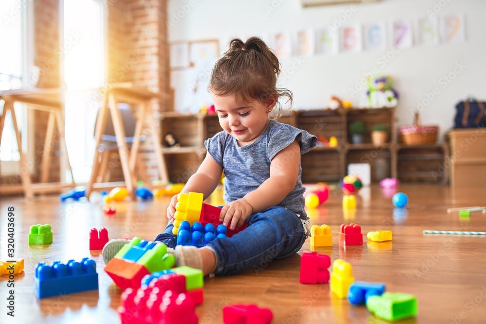 Beautiful toddler sitting on the floor playing with building blocks toys at kindergarten - obrazy, fototapety, plakaty 