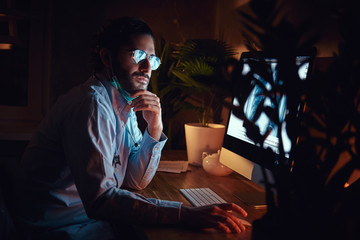 Wall Mural - Pensive radiologist is analysing the x-ray image using a computer on his night shift.