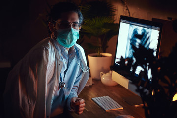 Wall Mural - On the night shift pensive doctor in protective mask is working with a x-ray image using a computer.