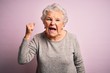 Senior beautiful woman wearing casual t-shirt standing over isolated pink background angry and mad raising fist frustrated and furious while shouting with anger. Rage and aggressive concept.