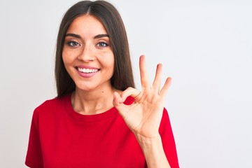 Wall Mural - Young beautiful woman wearing red casual t-shirt standing over isolated white background doing ok sign with fingers, excellent symbol