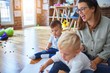 © Krakenimages.com - Beautiful teacher and group of toddlers sitting on the floor drawing using paper and pencil around lots of toys at kindergarten