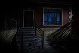 Fototapeta Na drzwi - Old house with a Ghost in the forest at night. Horror silhouette at the window. Old building in forest. Surreal lights. Horror Halloween concept