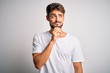 © Krakenimages.com - Young handsome man with beard wearing casual t-shirt standing over white background with hand on chin thinking about question, pensive expression. Smiling with thoughtful face. Doubt concept.